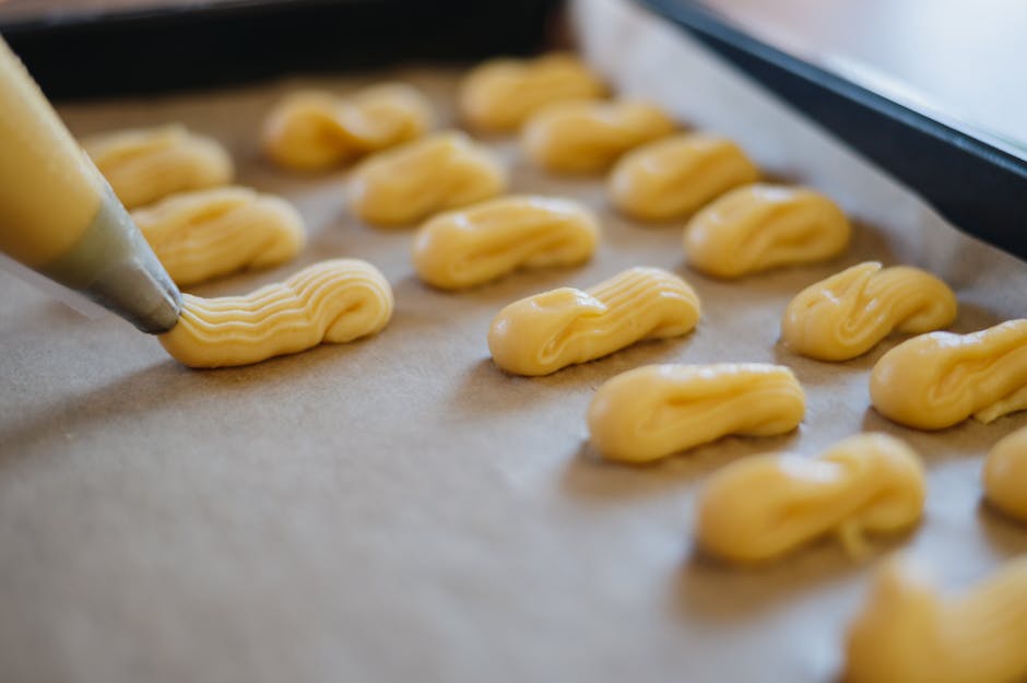 Mains pochant de la pâte à choux sur une plaque recouverte de papier sulfurisé